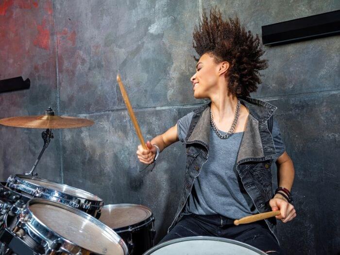 Young musician caught in the middle of drumming, her hands are raised with the stick in the air.