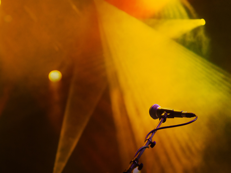 Photograph of a microphone against the background of yellow stage lights.