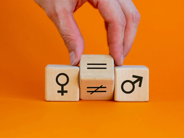 Hand turns a wooden cube and changes an unequal sign to an equal sign between symbols of men and women, on an orange background.