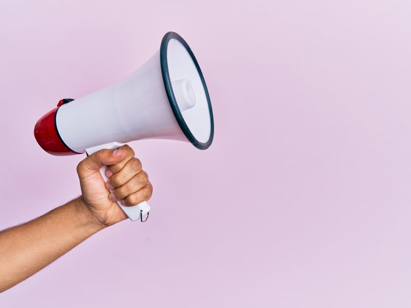 A hand holds up a megaphone against a lilac pink background