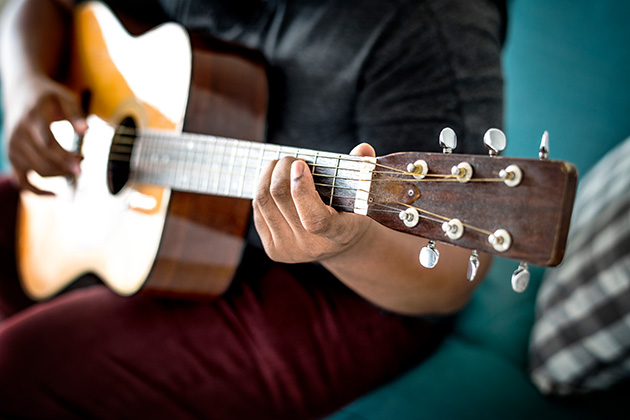 Photograph of a musician holding a guitar, we can't see their face and the photo focuses on their hands on the fretboard.