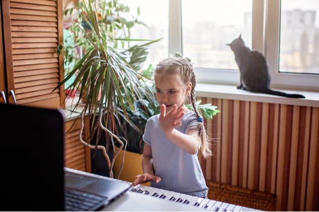 Child learning the keyboard, facing a computer where an online lesson is taking place.