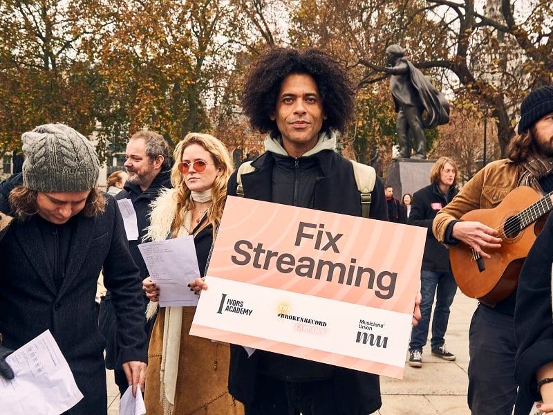 Campaigner holds a sign which reads Fix Streaming in a crowd of musicians at Parliament Square, London.