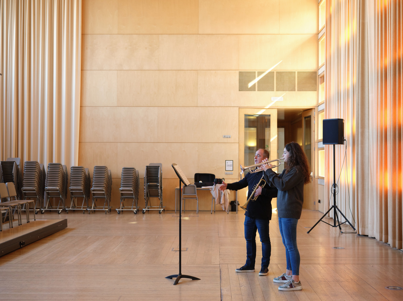 Photograph of a young person having a trumpet lesson, standing in a medium sized recital hall.