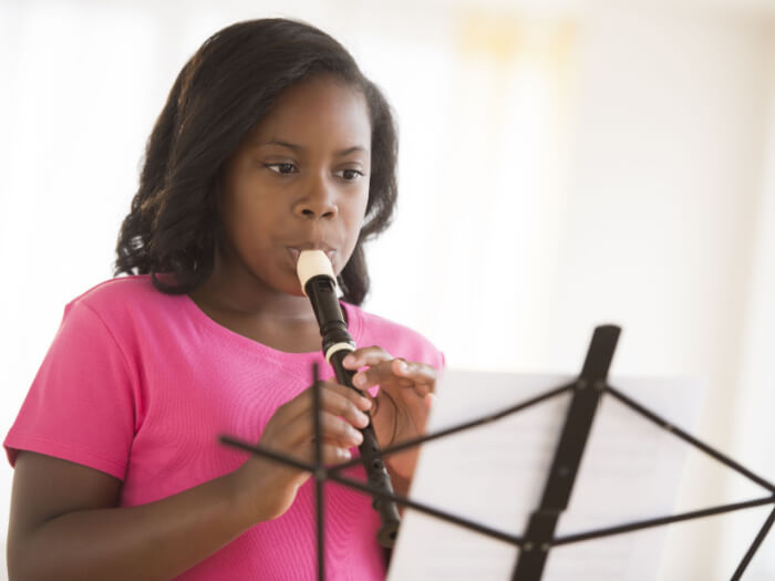 Child playing a recorder, reading intently from a music stand.