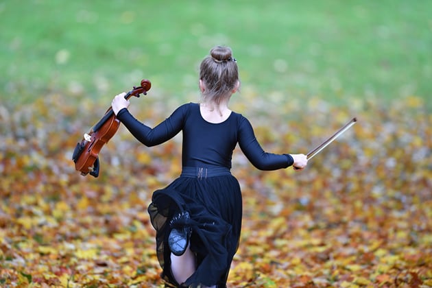 Photograph of child running through autumn leaves, holding a violin and bow