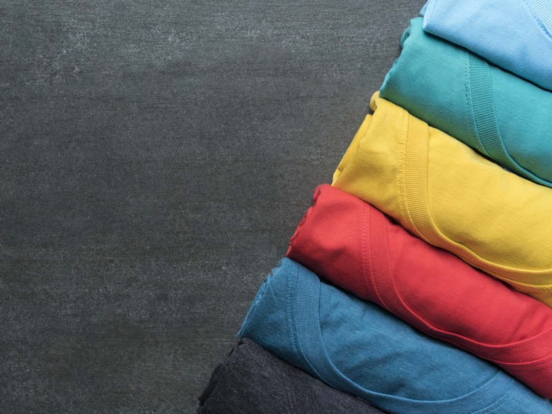 Photograph of a row of different brightly coloured t-shirts.