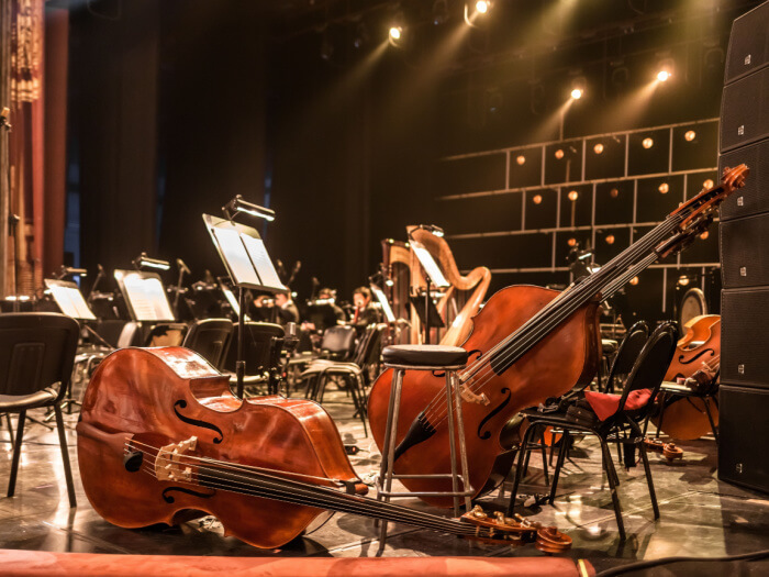 Instruments of a symphony orchestra stand unused on a lit stage, waiting for players