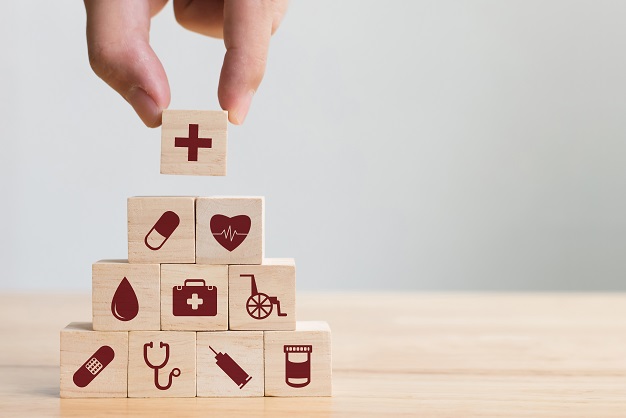 Small wooden blocks stacked in a tower, each one with a symbol representing different aspects of healthcare.