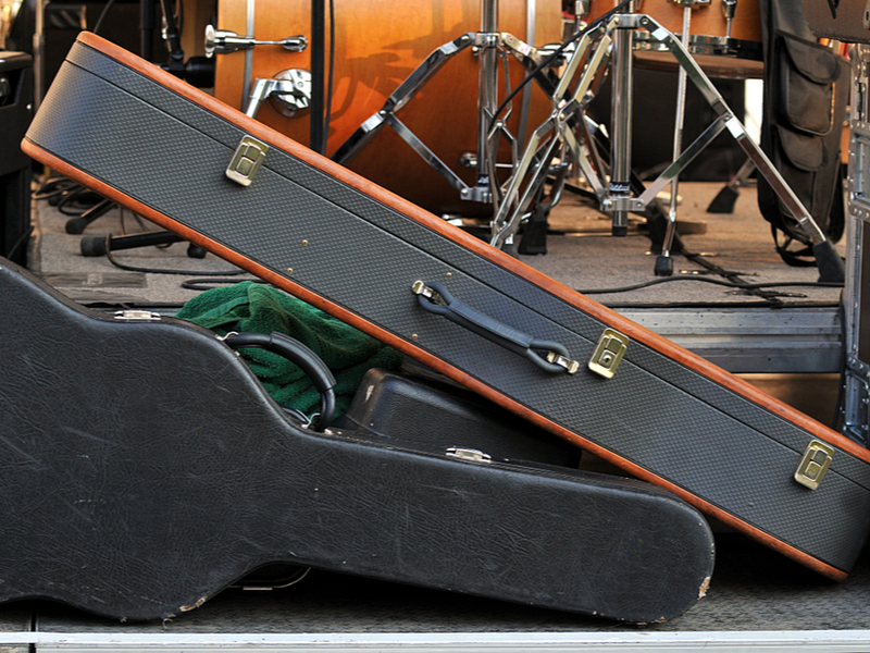 A number of instruments in hard cases proped at the side of a stage, looking slightly chaotic.