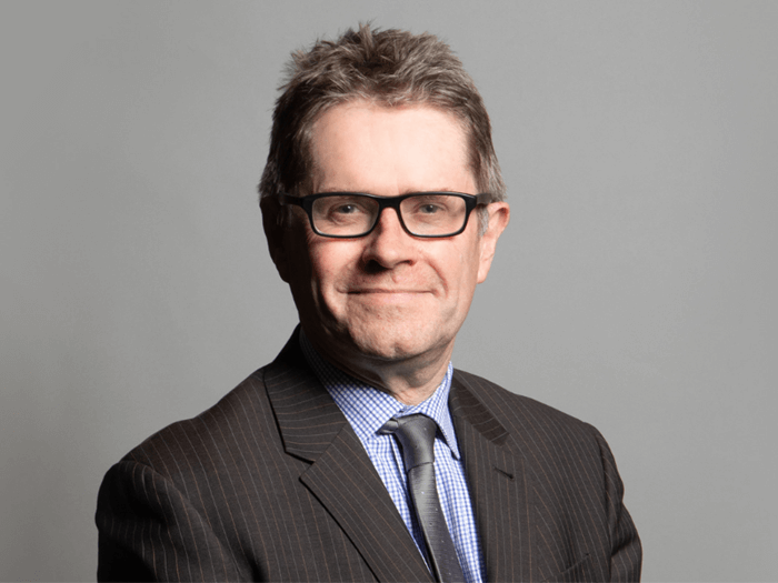 Official portrait of Kevin Brennan MP. Kevin has short brown hair and is wearing glasses, a dark brown striped suit and blue shirt with brown tie.
