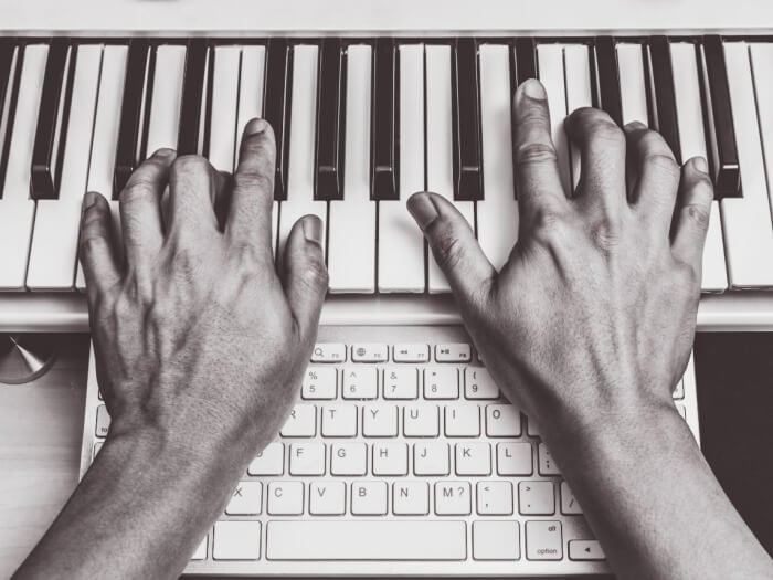 Pair of hands on a computer keyboard and a piano keyboard.