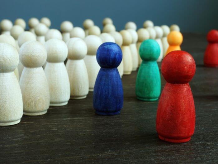 Inclusion and discrimination concept. Lines of wooden figurines as a barrier in front of different coloured figurines.