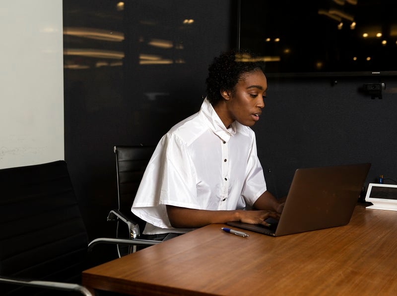 Photograph of a person using a laptop working at a table in an office.