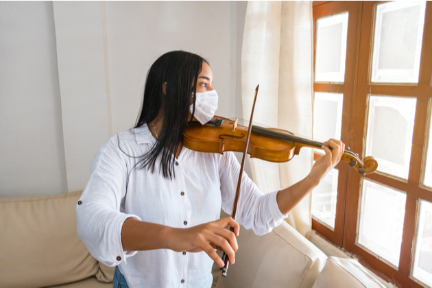 Young adult playing violin in isolation, wearing a surgical mask as encouraged by the Government in public spaces