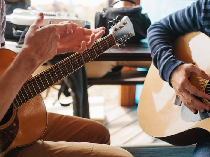 Close up of two people sat with acoustic guitars representing music lessons.