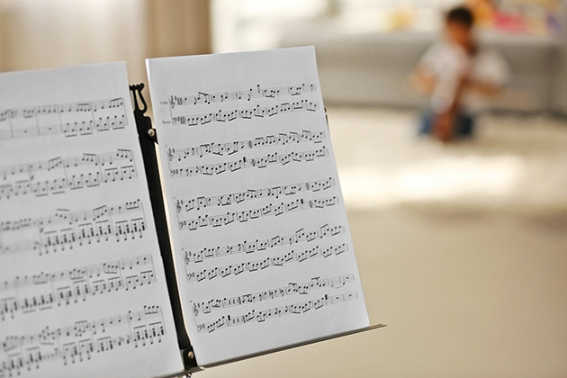 Photograph of sheet music on stand, with blurred cello student in the background