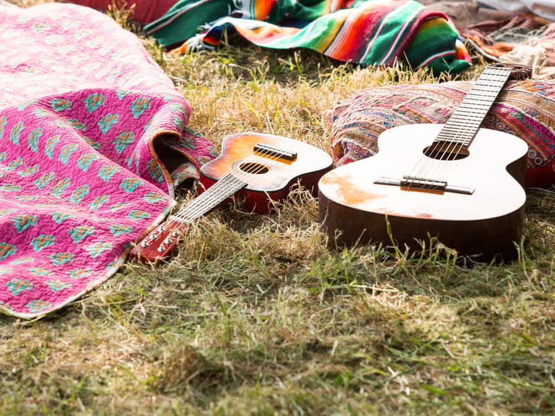 Two guitars resting in the grass amongst various objects like blankets and colourful pillows which indicate a festival campsite.