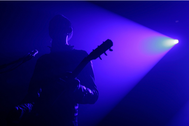 Photograph of a musician playing a guitar, the heavy blue light means we can't clearly see the performer.