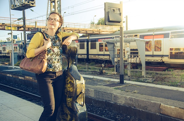 Photograph of a musician standing at a train station with a cello