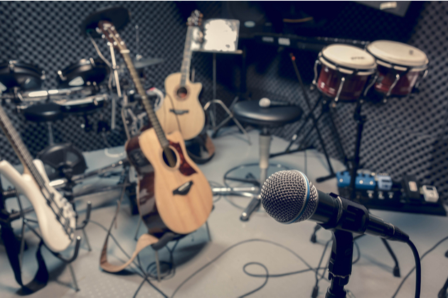 Photograph of a number of instruments, including an acoustic guitar and percussion, propped around a recording studio with various microphones.