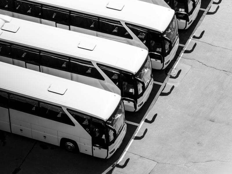 Black and white photo of a row of large your busses at a stand still.