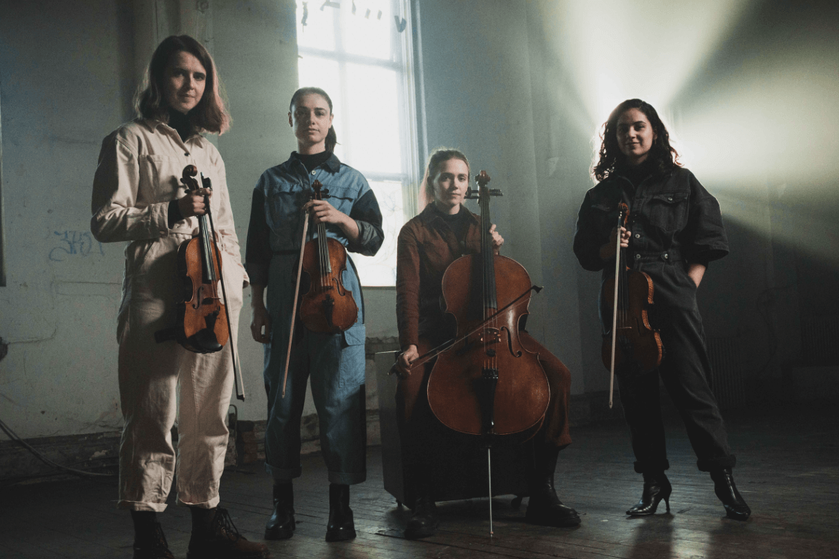 Vulva Voce standing in a dimly lit room holding their instruments.