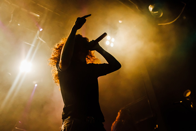 Photograph of a singer, who we can not clearly see, silhouetted against bright stage lights on a smokey stage.