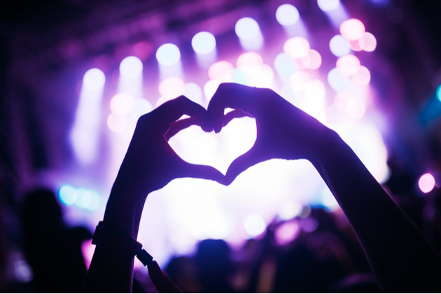 A music fan at the concert holding their hands in the heart shape