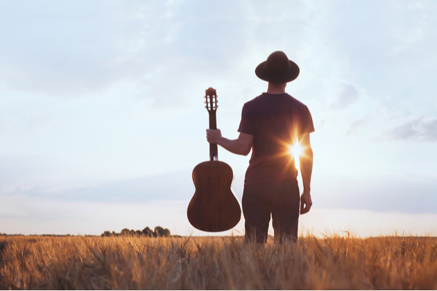 A man with a guitar standing in the field against the sunlight