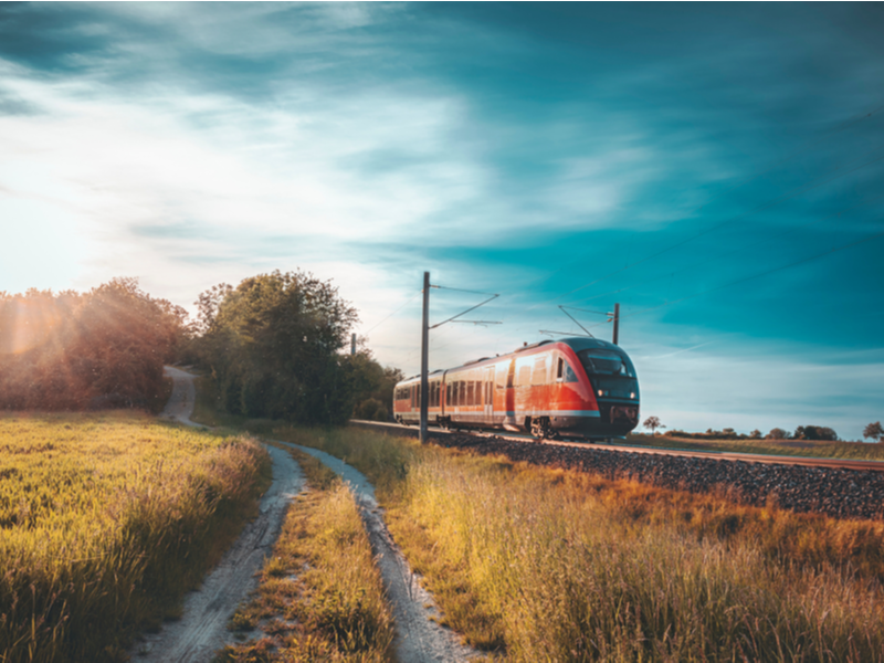 A German red train running in hazy dusky light through a field of yellowy green grass.