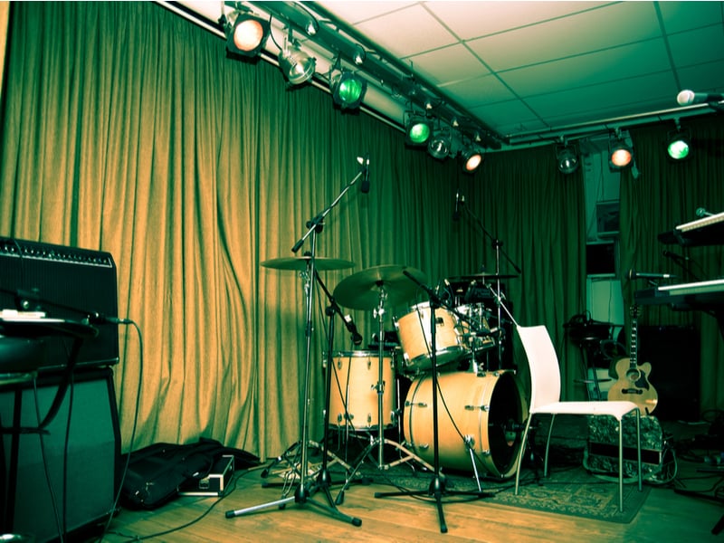 Photograph of a small, empty stage, with drum set, microphone and amplifier set up to play.