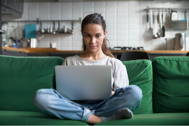 A woman sitting with a laptop on a sofa at home